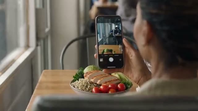 A person photographing a grain bowl at a restaurant table